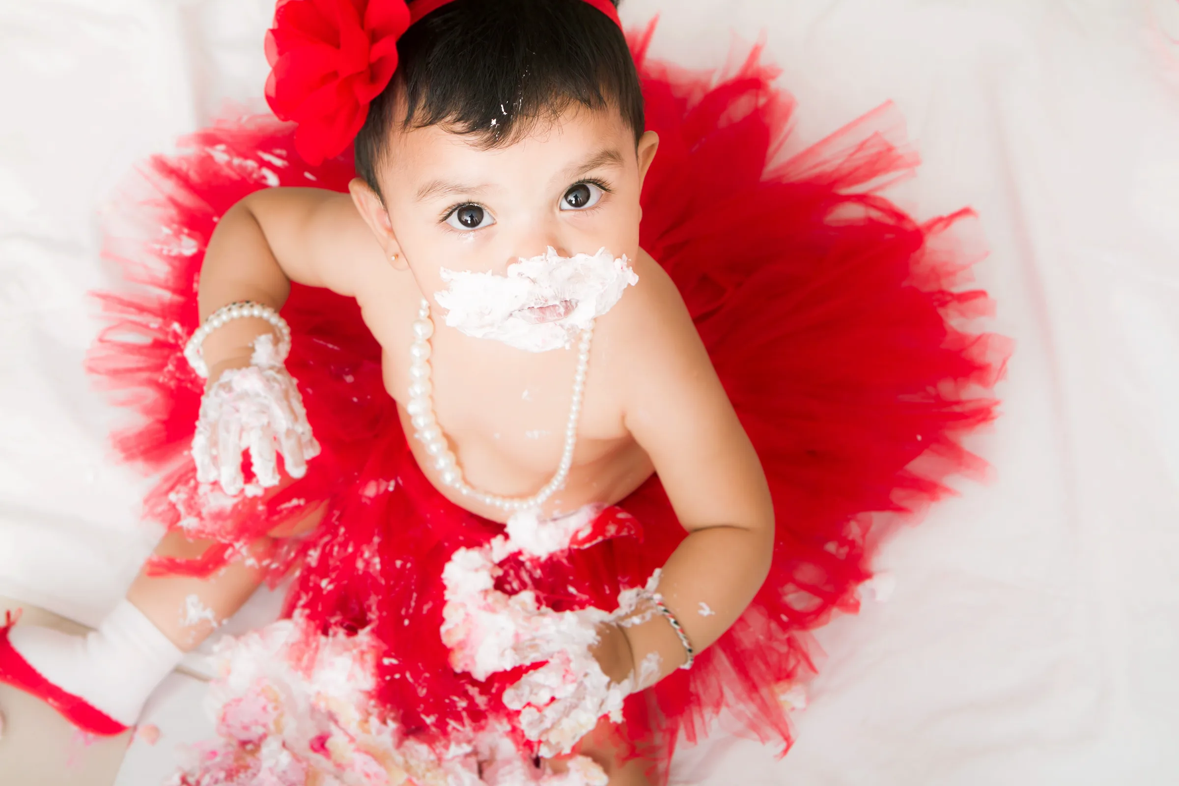 Baby in a red tutu covered in cake at a first birthday cake smash, photographed from above by Vivek Pankaj