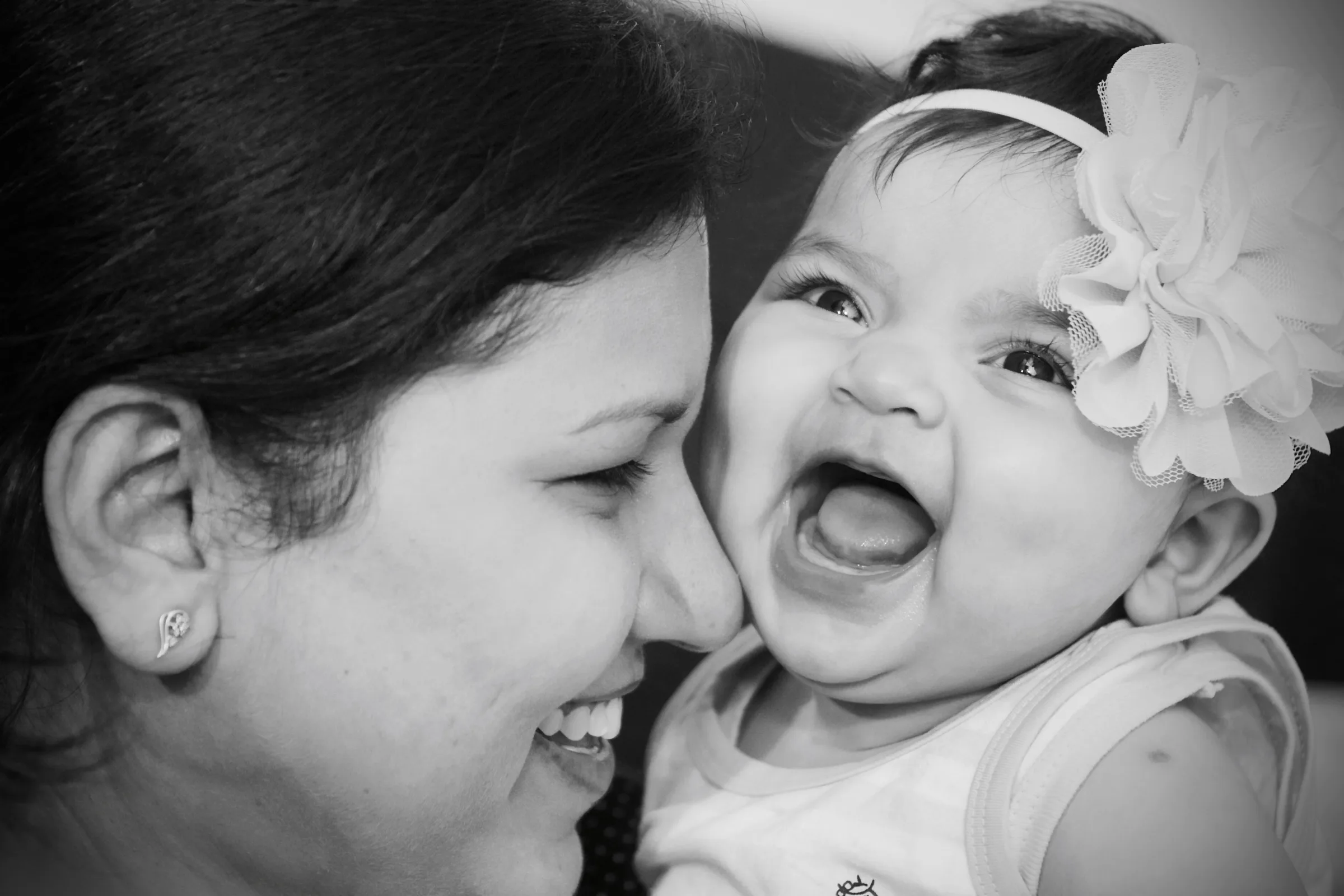Black and white close-up of a mother cheek to cheek with her laughing baby daughter, family photography by Vivek Pankaj
