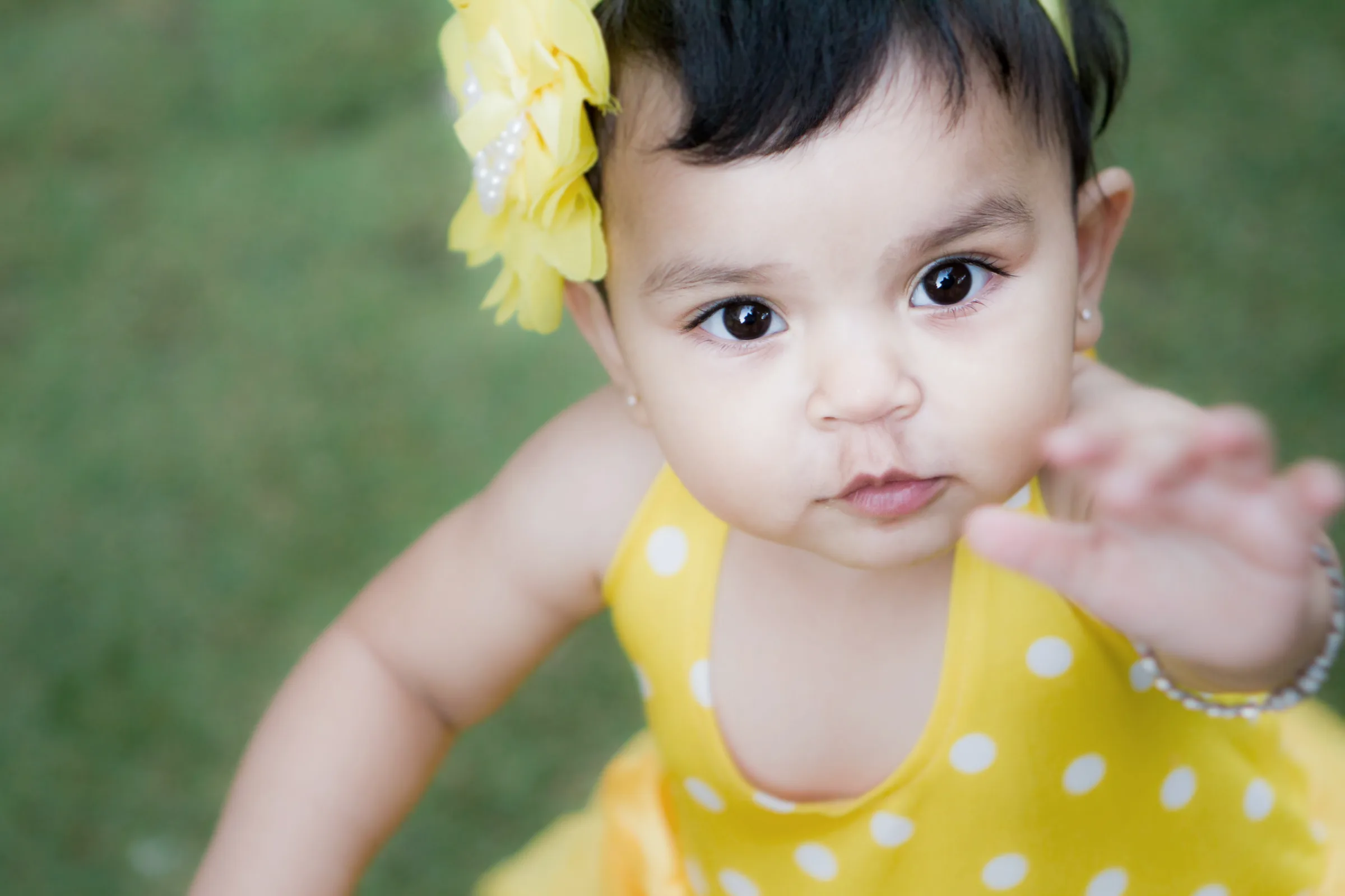 Close-up of a baby girl with a yellow flower hair clip reaching towards the camera, kids photography by Vivek Pankaj