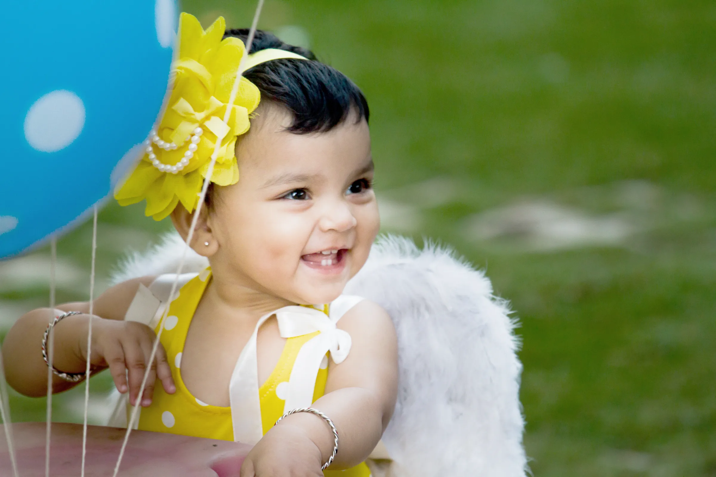 Laughing baby girl in a yellow polka-dot dress with angel wings and balloons on the lawn, kids photography by Vivek Pankaj