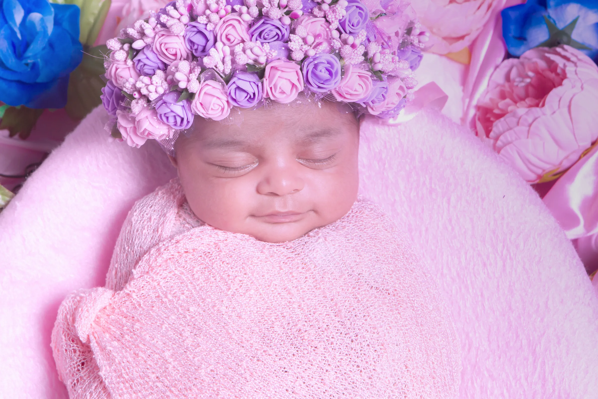 Sleeping newborn in a pink flower crown and soft pink wrap among pastel roses, newborn photography by Vivek Pankaj
