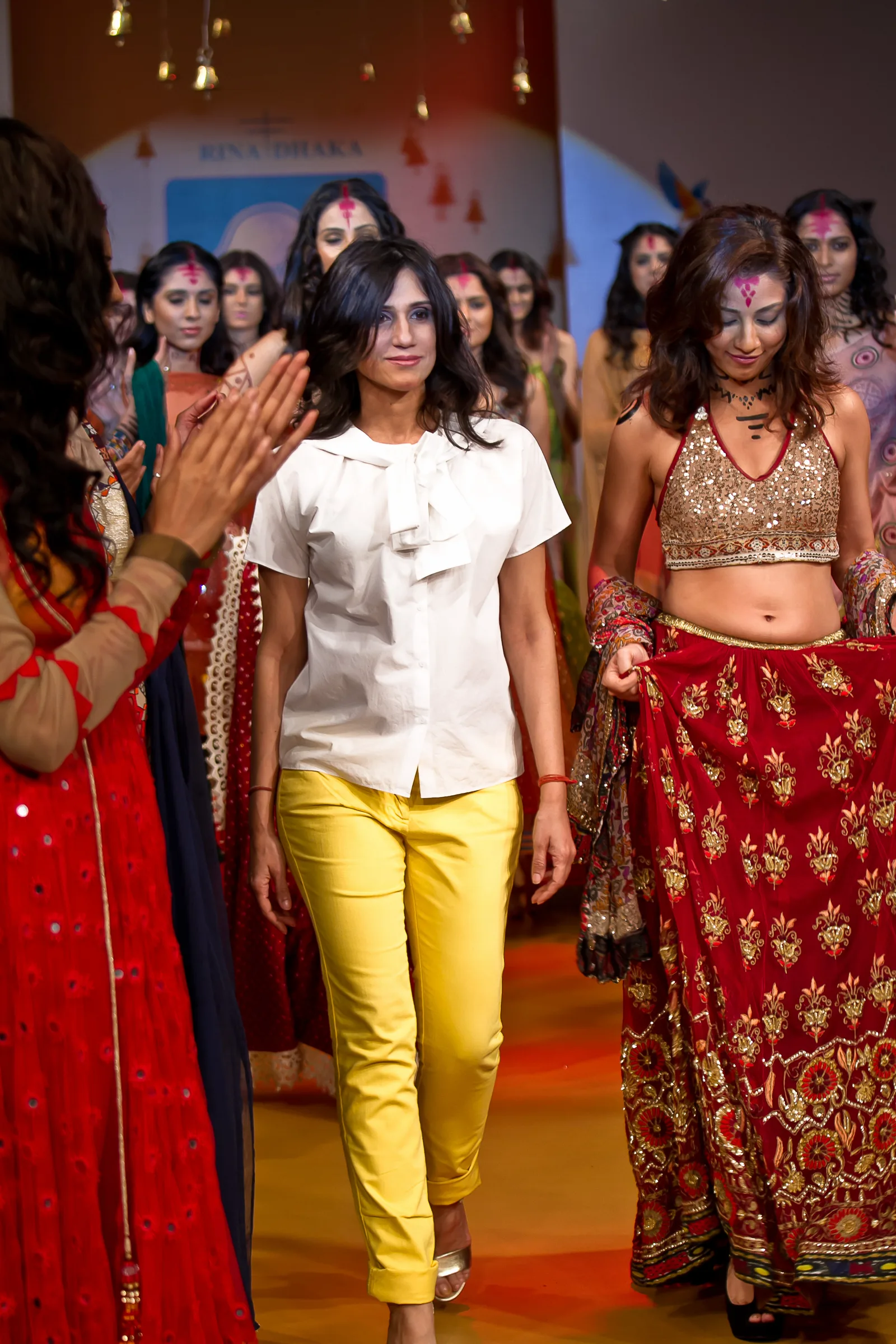Designer in a white shirt walking the Bangalore Fashion Week finale with models in red and gold lehengas, photographed by Vivek Pankaj