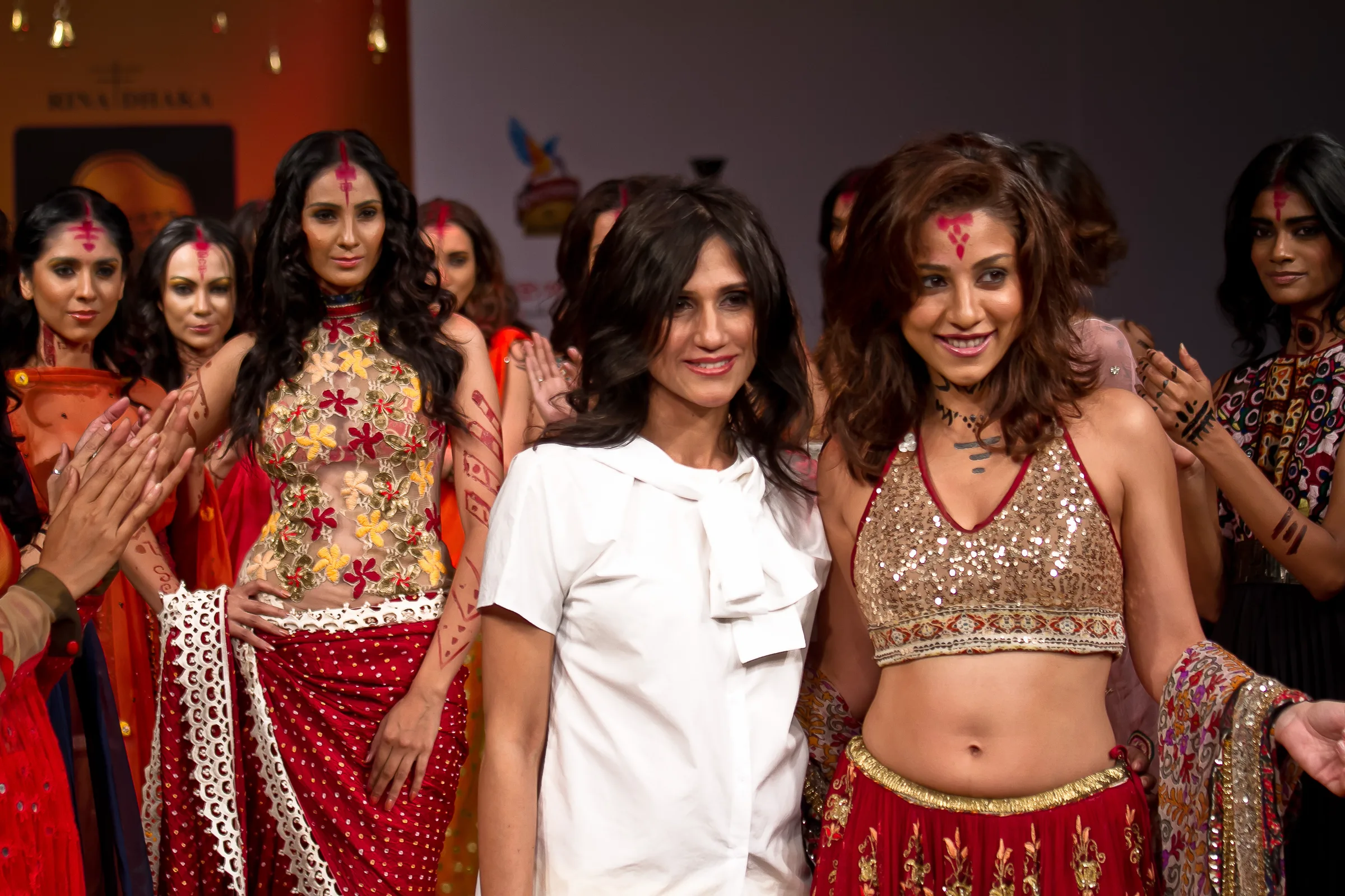 Designer in white celebrating with models in embroidered lehengas at the Bangalore Fashion Week finale, photographed by Vivek Pankaj