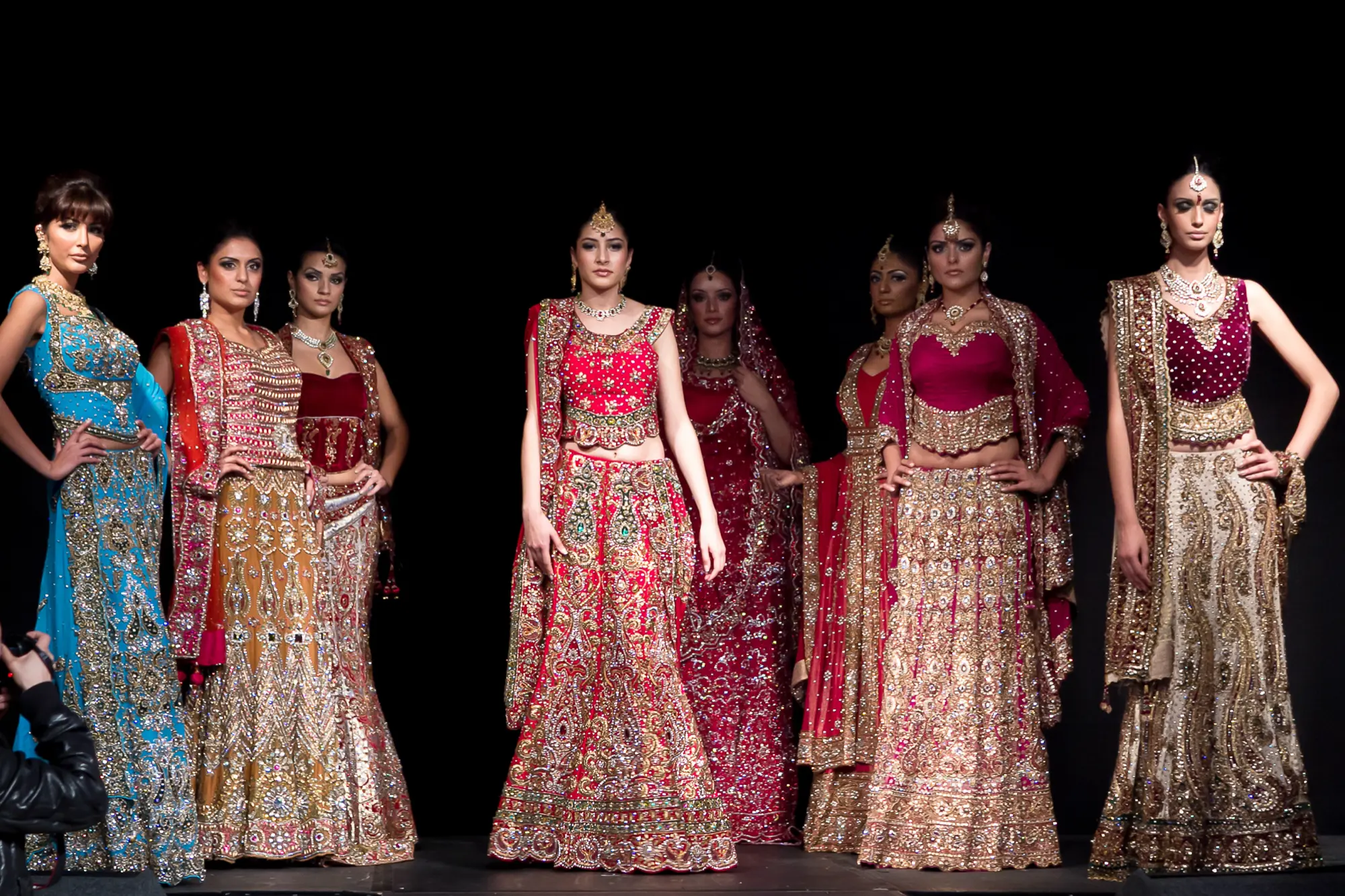 Line of models in embroidered bridal lehengas lit against a dark stage at the Bangalore Fashion Week finale, photographed by Vivek Pankaj