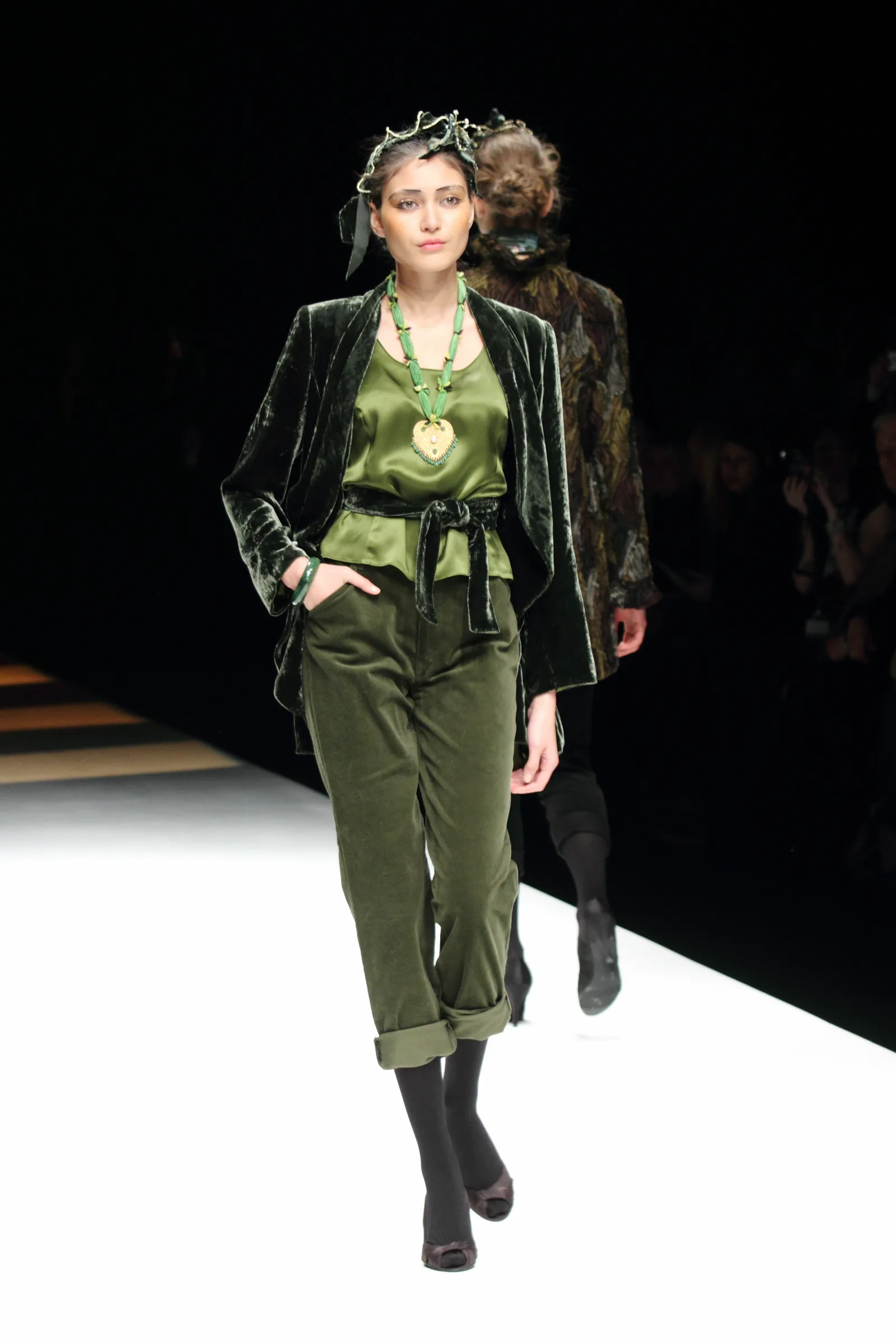 Model in a green velvet jacket and cropped trousers walking a white runway, photographed by Vivek Pankaj