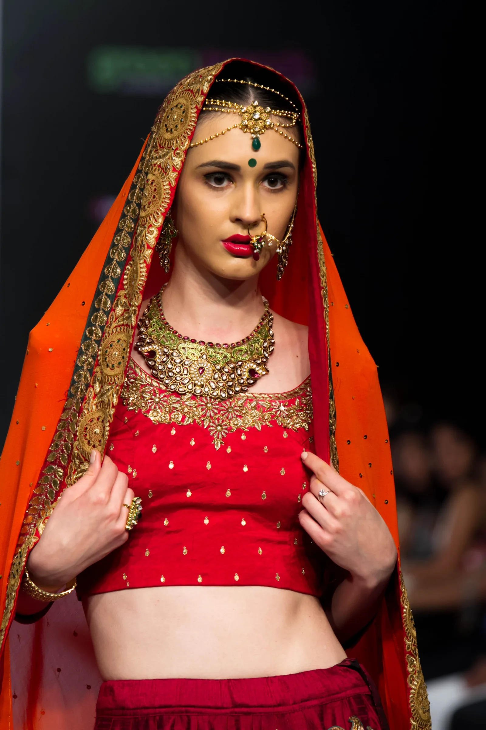 Model in a red embroidered choli, gold necklace and nose ring under an orange dupatta at Bangalore Fashion Week, photographed by Vivek Pankaj