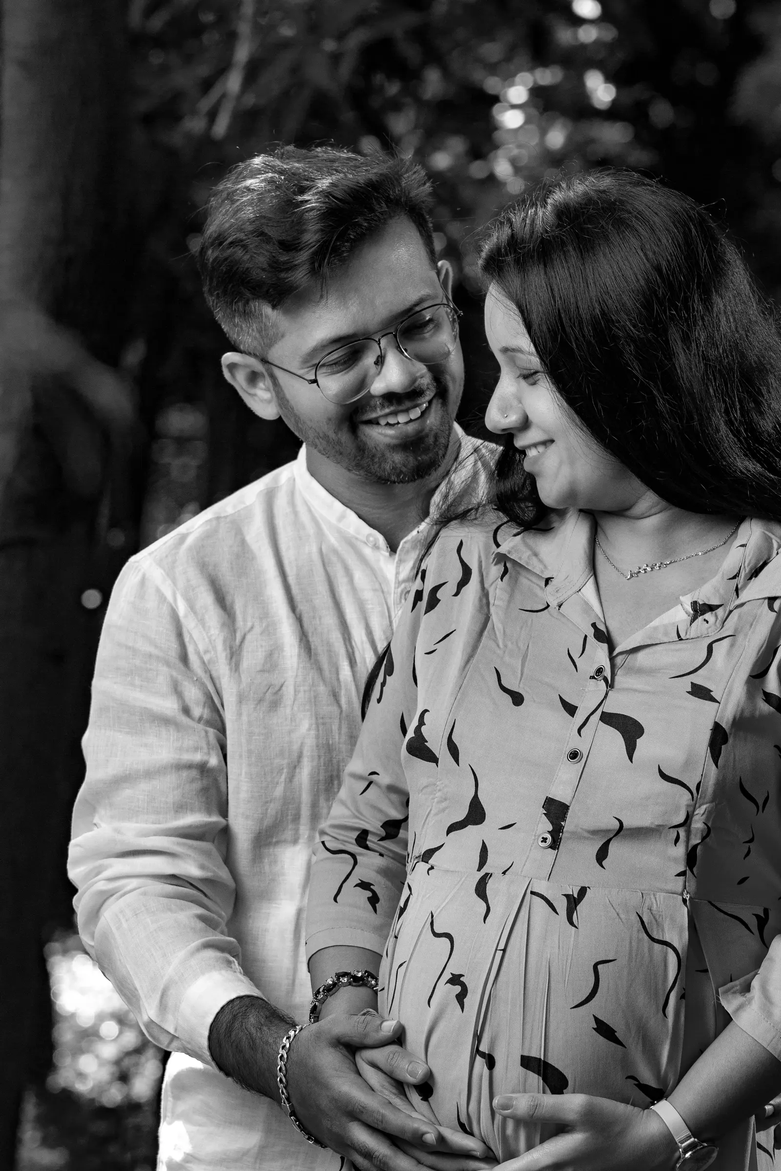Black and white portrait of an expecting couple smiling, his hands over hers on the bump, maternity photoshoot by Vivek Pankaj