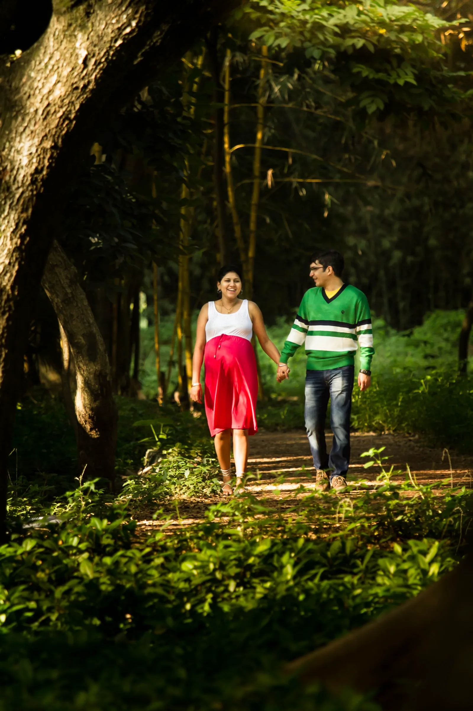 Couple walking hand in hand along a leafy forest path during a maternity shoot by Vivek Pankaj