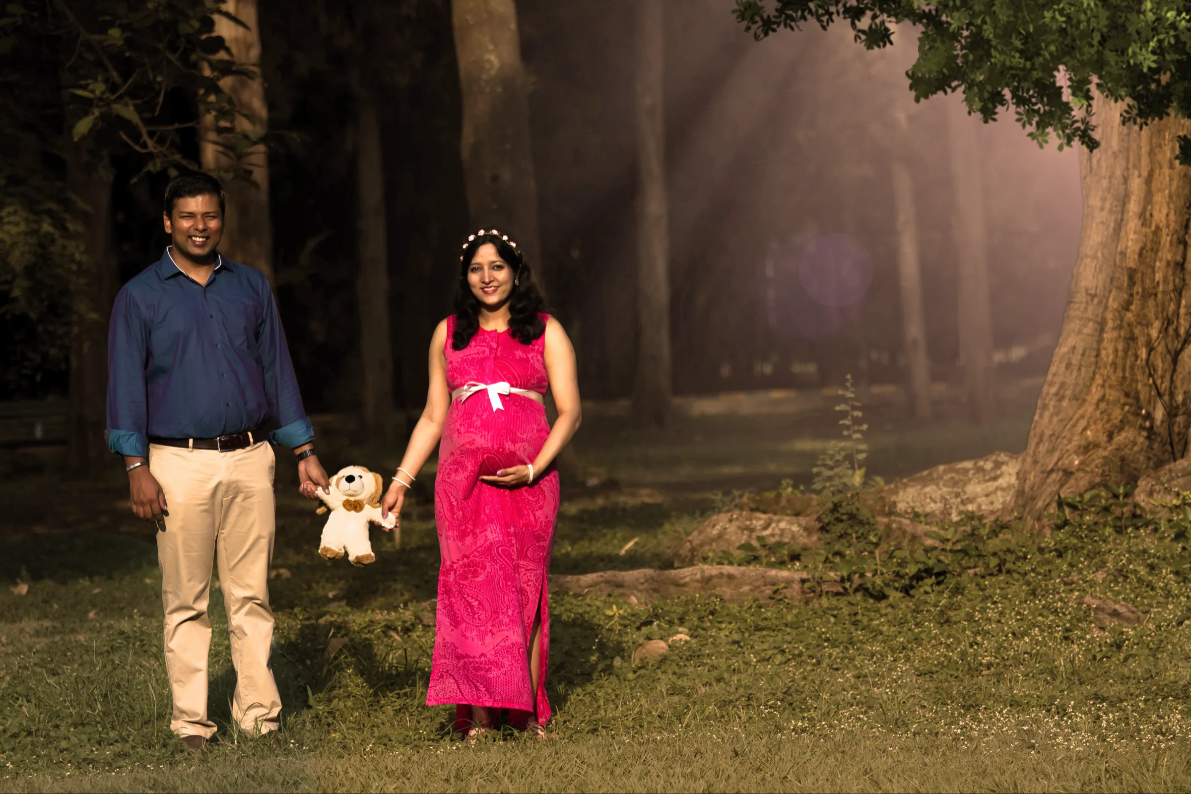 Expecting couple in a sunlit woodland with a teddy bear, maternity photography by Vivek Pankaj