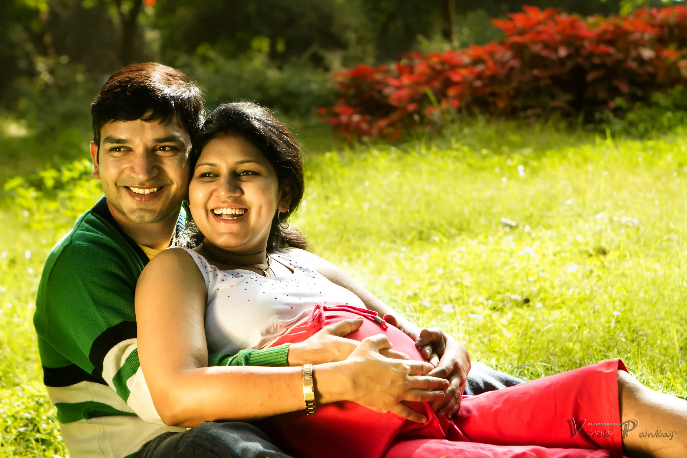 Laughing couple lying on the grass, her head on his shoulder and his hand on the bump, maternity shoot by Vivek Pankaj