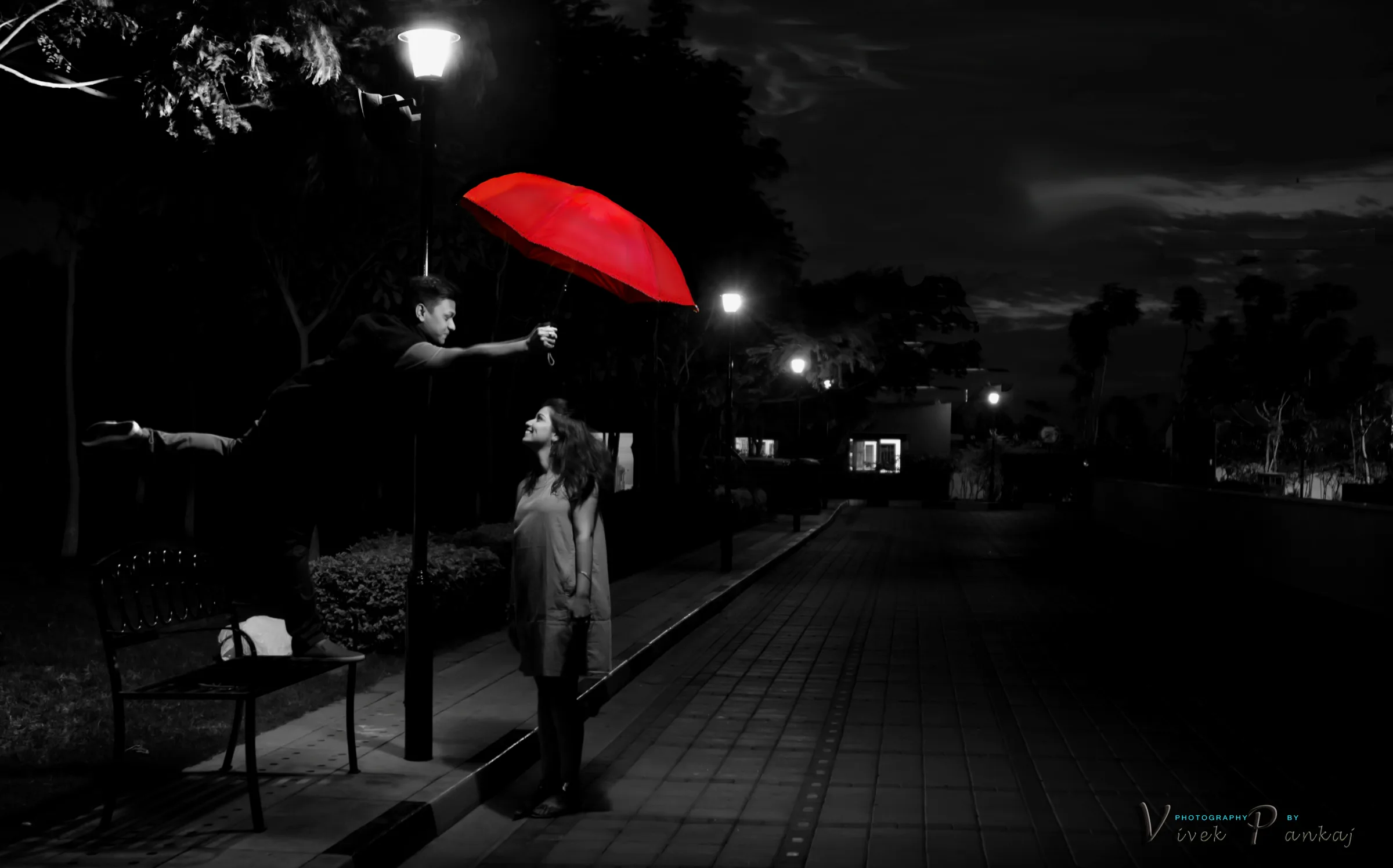 Couple under a red umbrella on a lamp-lit path at night, black and white with a red accent, pre-wedding photography by Vivek Pankaj